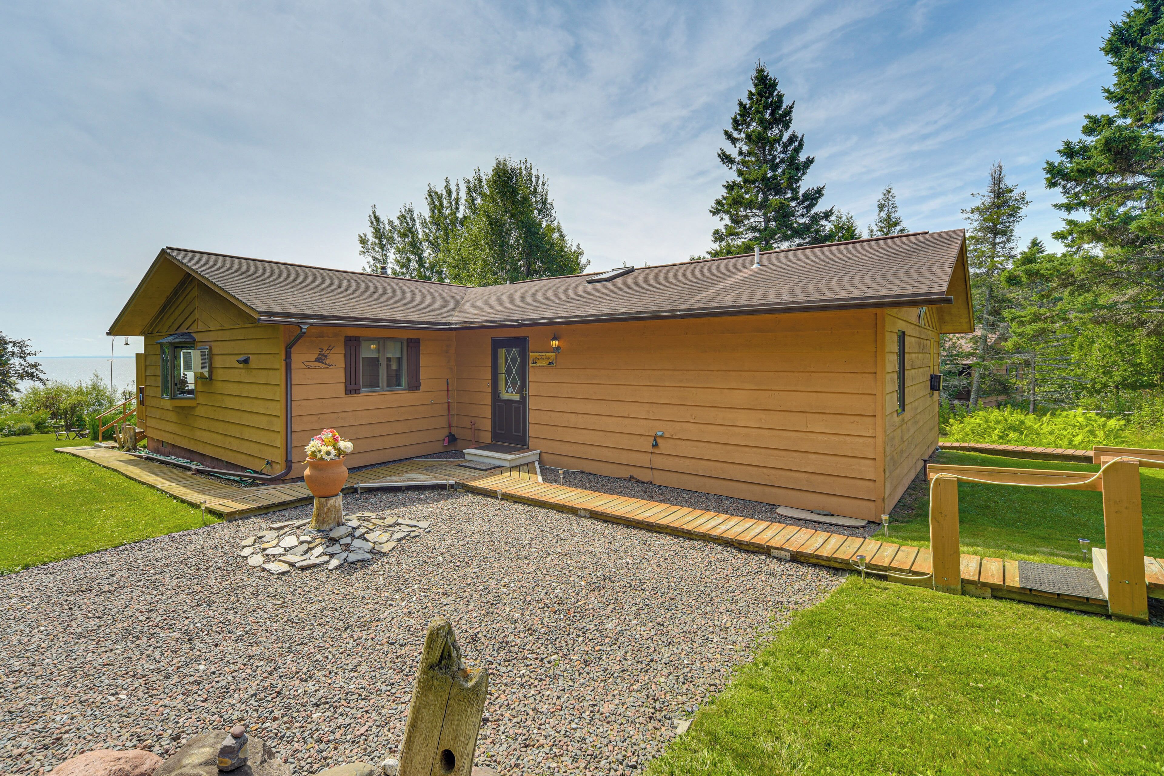 Une petite maison en bois d’un seul étage, avec une allée en gravier et une terrasse en bois.