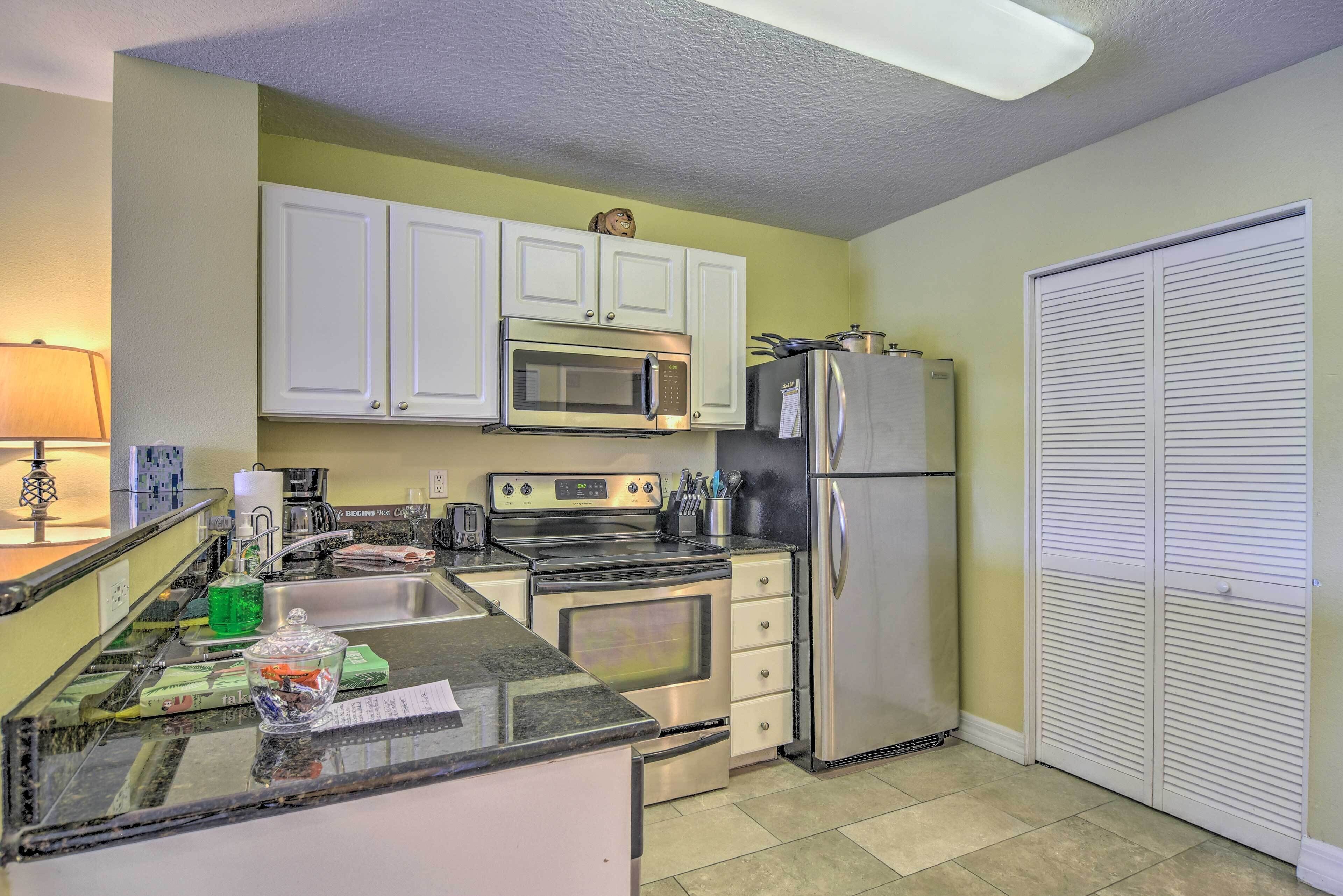 A compact kitchen with white cabinets, a stainless steel refrigerator, a microwave, and an oven.