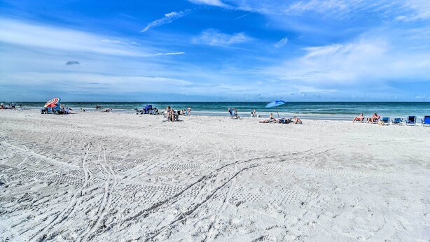 A beach with clear skies, people relaxing, and a few umbrellas.