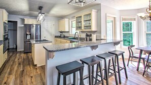 Cozinha moderna com ilha central, banquetas de bar e área de refeições com lustre.