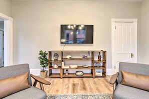Ein Wohnzimmer mit zwei grauen Sofas, einem Holzregal, einem Flachbildfernseher und einem gemusterten Teppich.