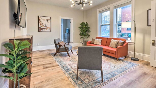 Un salon avec une grande fenêtre, un canapé, un fauteuil, un tapis et une plante.