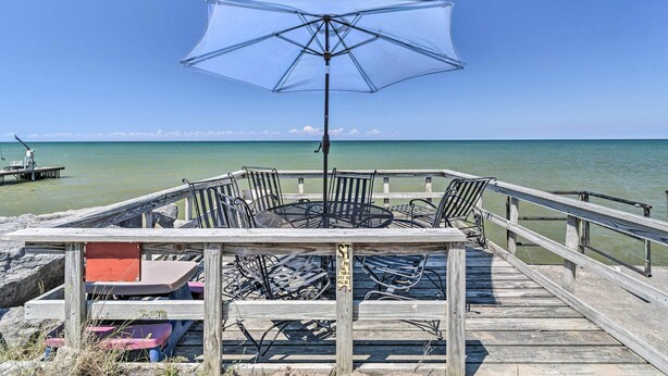 Une terrasse en bois avec une table et des chaises, un parasol et une vue sur l’océan.