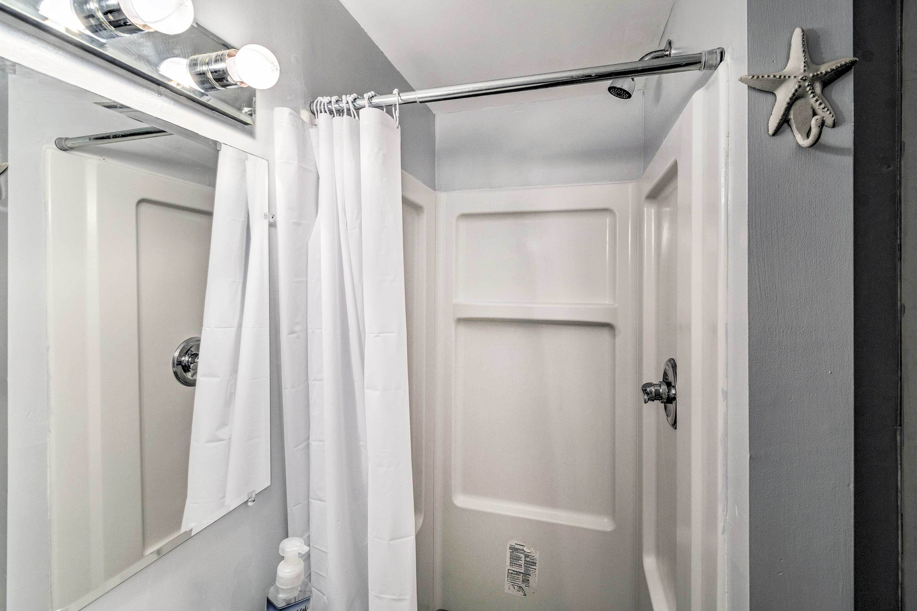 A bathroom with a shower curtain, a mirror with lights, a starfish decoration, and a door.