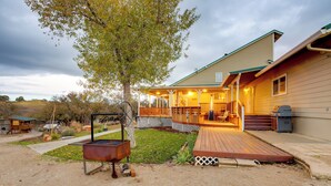 Ein Haus mit überdachter Veranda, Grill und Baum im Garten.
