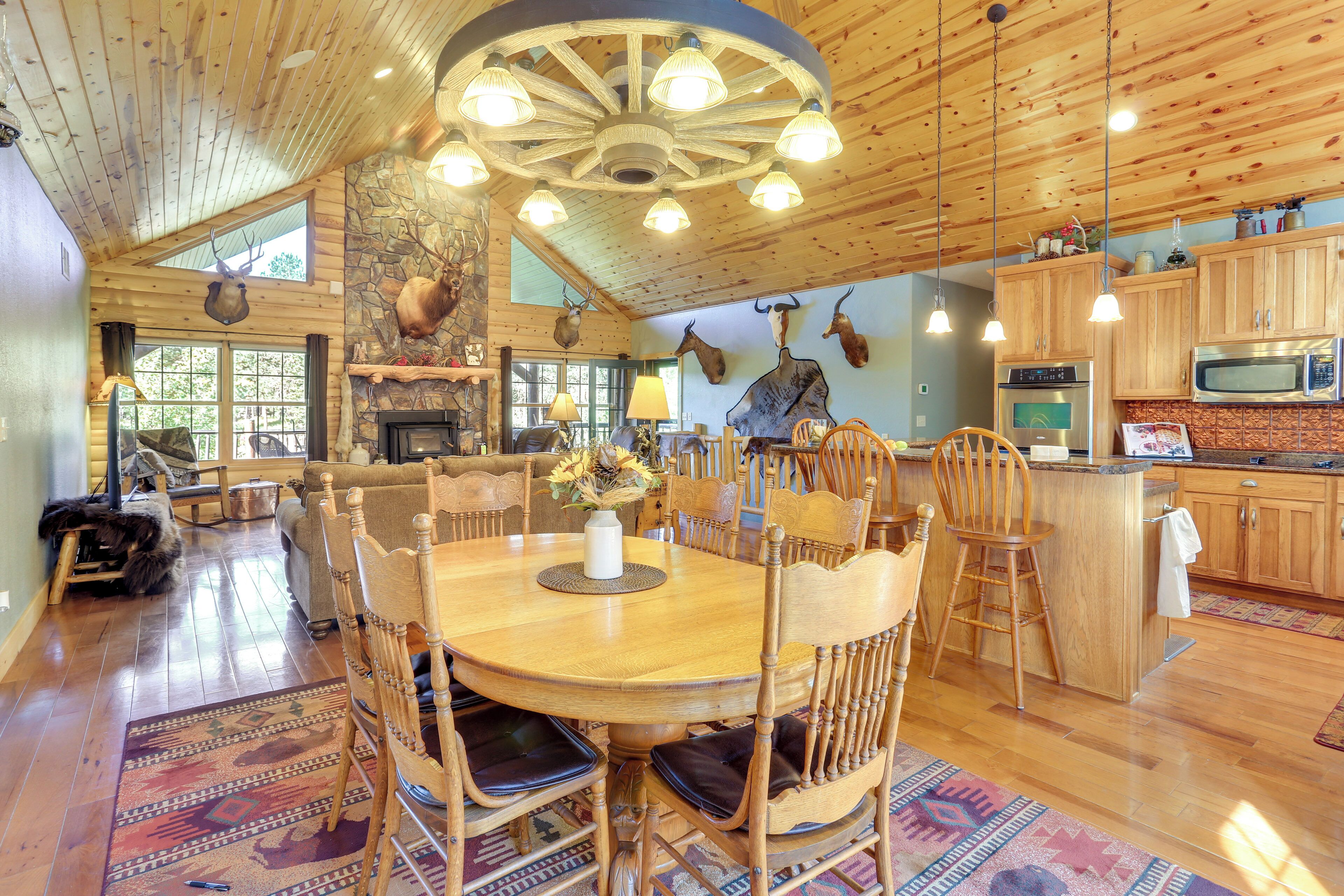 A spacious dining area with a wooden table and chairs, a stone fireplace, and a ceiling with wooden beams and lights.