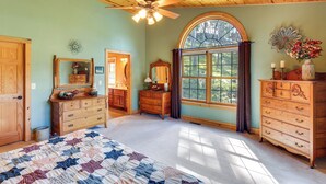 Un dormitorio con una cama grande, muebles de madera, un ventilador de techo y una ventana con cortinas.