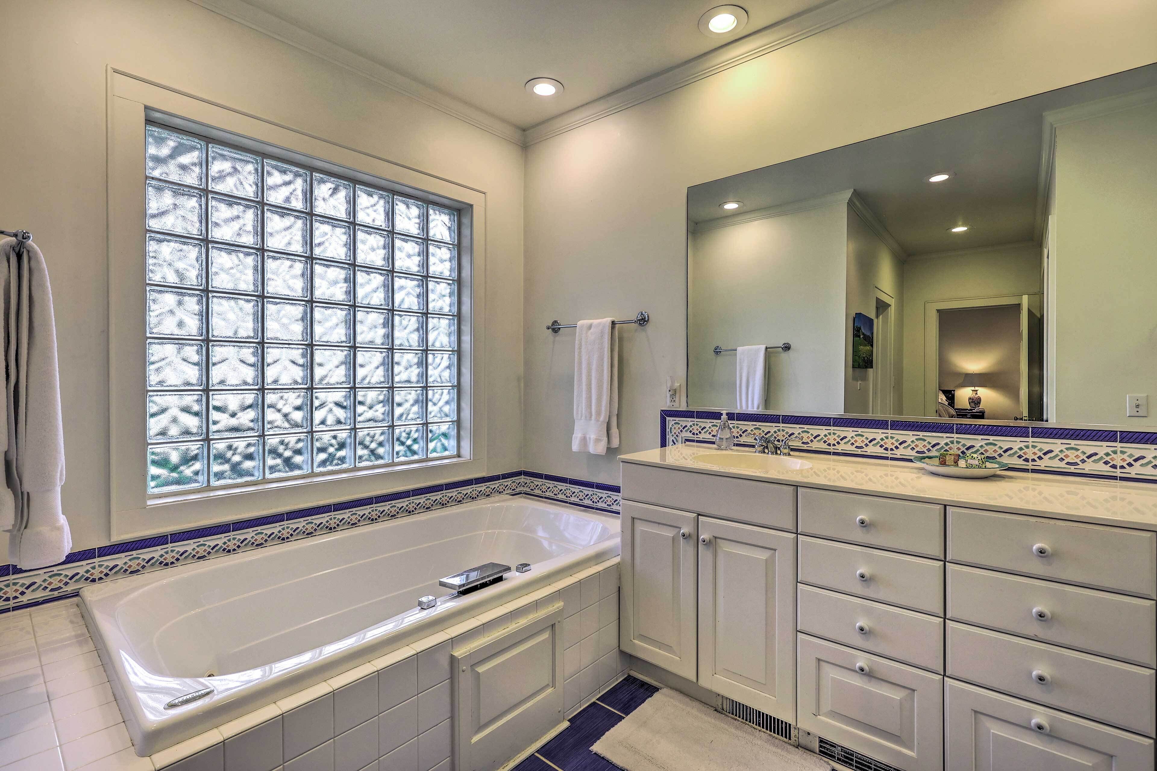 Une salle de bain moderne avec une grande baignoire, un meuble-lavabo avec des tiroirs, un miroir et une fenêtre en verre dépoli.