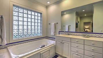 Une salle de bain moderne avec une grande baignoire, un meuble-lavabo avec des tiroirs, un miroir et une fenêtre en verre dépoli.