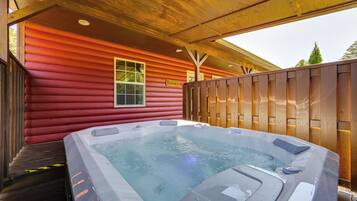 Un jacuzzi frente a una cabaña de madera roja con terraza de madera y ventana.