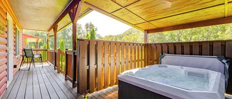 A wooden deck with a hot tub, wooden railings, and a view of trees.