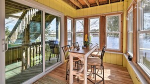 A sunlit dining area with a wooden table and chairs, large windows, and a view of the outdoors. - High-end Canal Front Paradise in Kill Devil Hills (Kill Devil Hills)