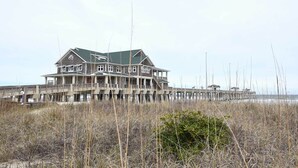 A large, multi-story beachfront house with a pier extending into the water. - High-end Canal Front Paradise in Kill Devil Hills (Kill Devil Hills)