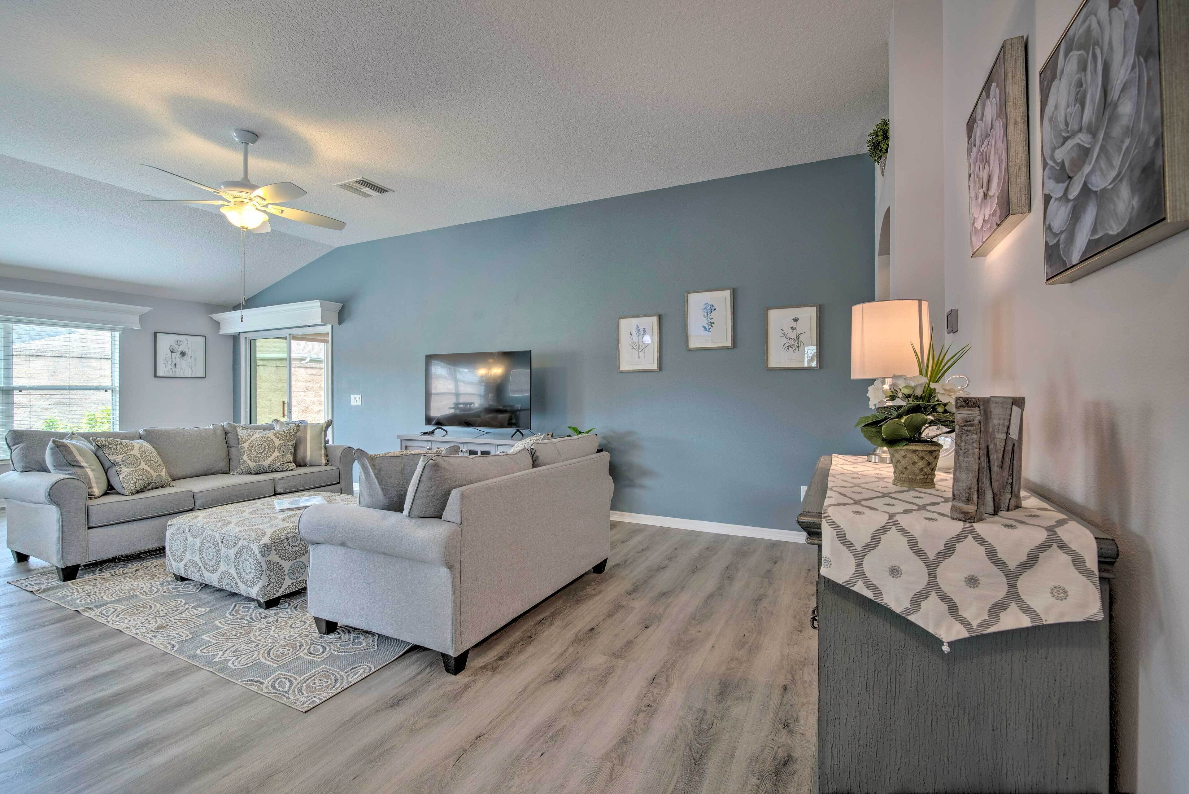 A modern living room with a grey sofa set, a TV, and a decorative table with a lamp.