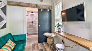 Un salon moderne avec un canapé de couleur turquoise, un plafond en bois, une porte noire à motifs chevrons, un téléviseur fixé au mur et une petite table sur laquelle est posée une plante.