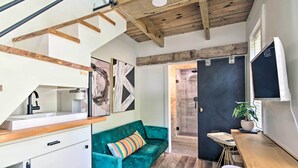 Une cuisine moderne avec un plan de travail en bois, un canapé turquoise agrémenté d’un coussin à rayures et une porte noire donnant accès à une cabine de douche.