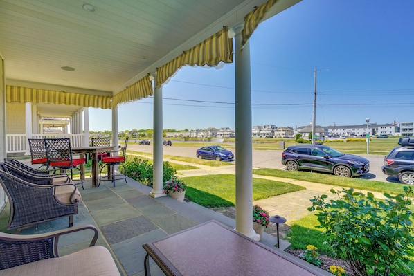 A covered porch with outdoor seating, a view of a parking lot, and a clear sky.
