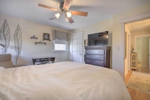 A bedroom with a large bed, a ceiling fan, a TV, a dresser, and a desk.