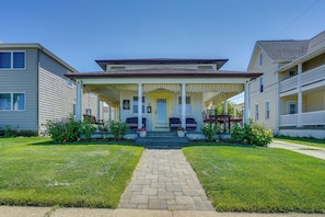 A two-story house with a front porch, a brick pathway leading to the entrance, and a small garden area with potted plants.