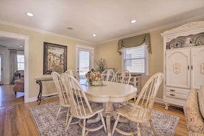 A dining area with a round table surrounded by six chairs, a floral centerpiece, and a white cabinet with decorative plates.