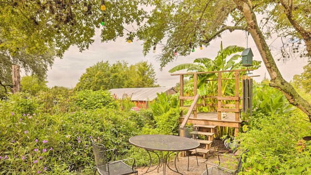 Een patio in de tuin met een metalen tafel en stoelen, omgeven door weelderige begroeiing en een houten constructie.