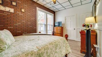 A bedroom with a brick wall, a wooden bed, a ceiling fan, a dresser, and a television.