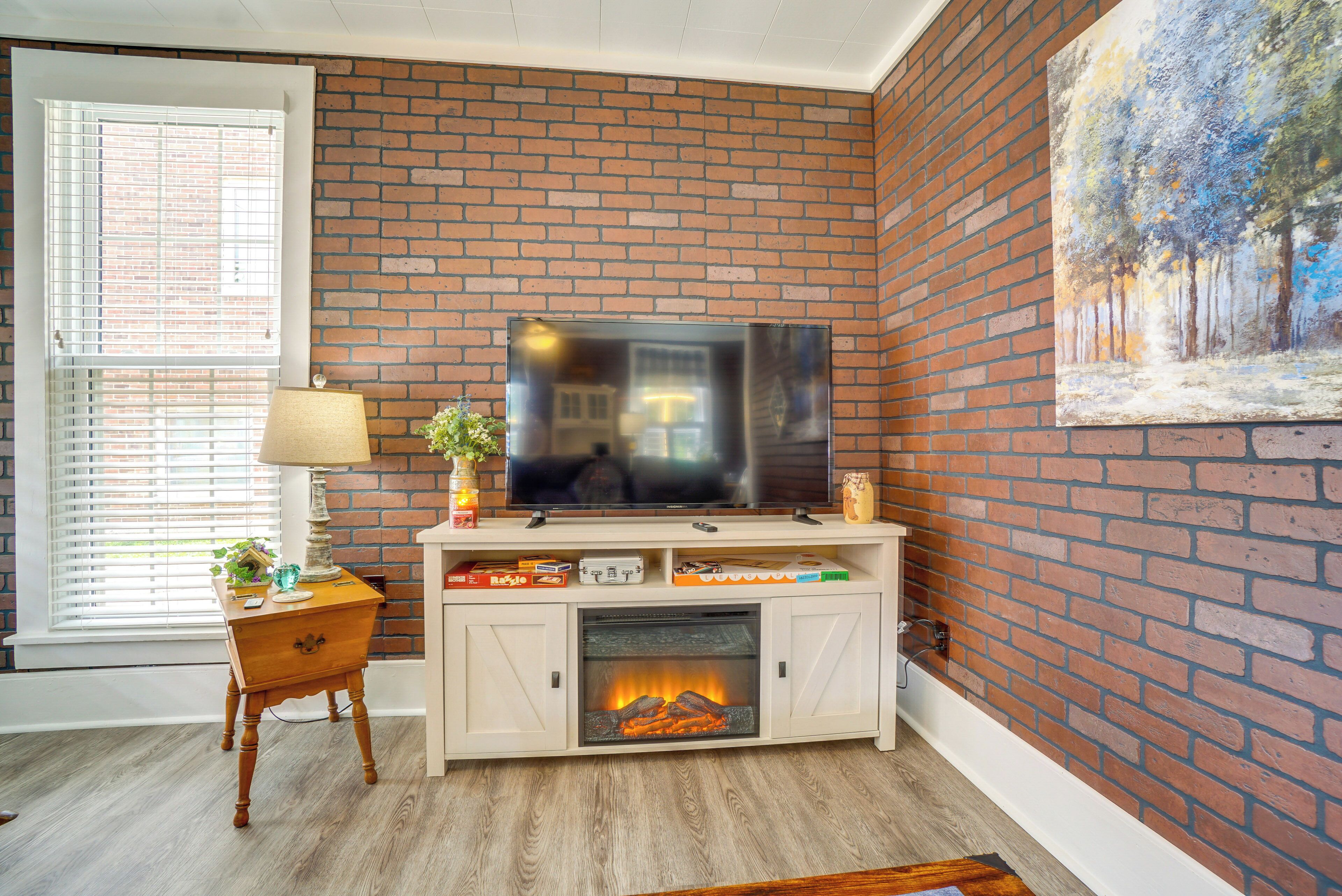 A living room with a brick wall, a television, a fireplace, and a painting.