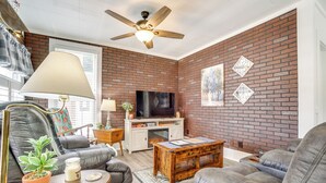 Ein Wohnzimmer mit Backsteinwand, Deckenventilator, Fernseher und Kamin.