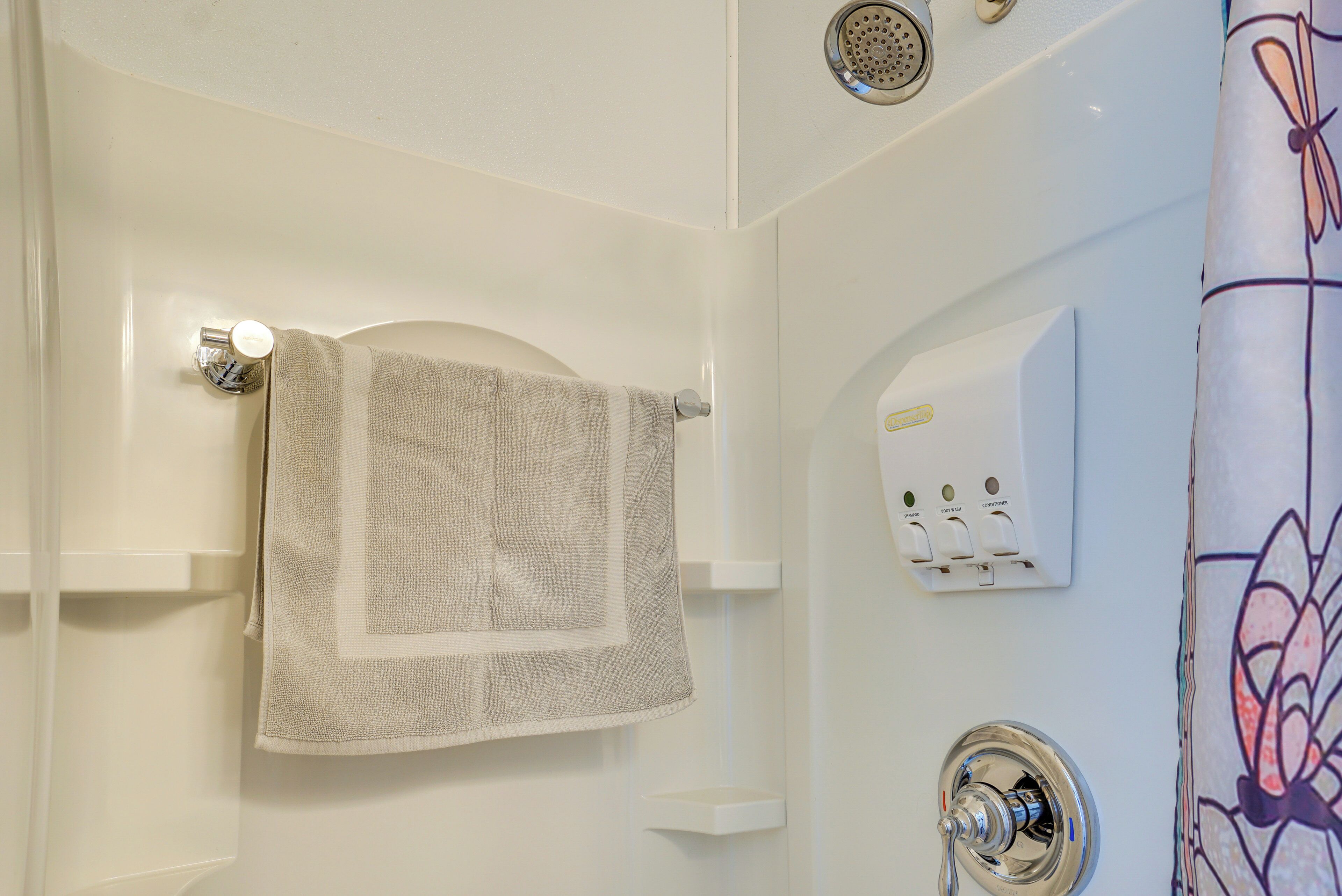 Un bagno con un asciugamano appeso a un portascopevoli, un soffione e un pannello di controllo con diversi pulsanti.