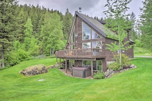 A cabin with a deck, surrounded by a lush green landscape and dense forest. - Quiet + Elegant Whitefish Home w/ Hot Tub (Whitefish)