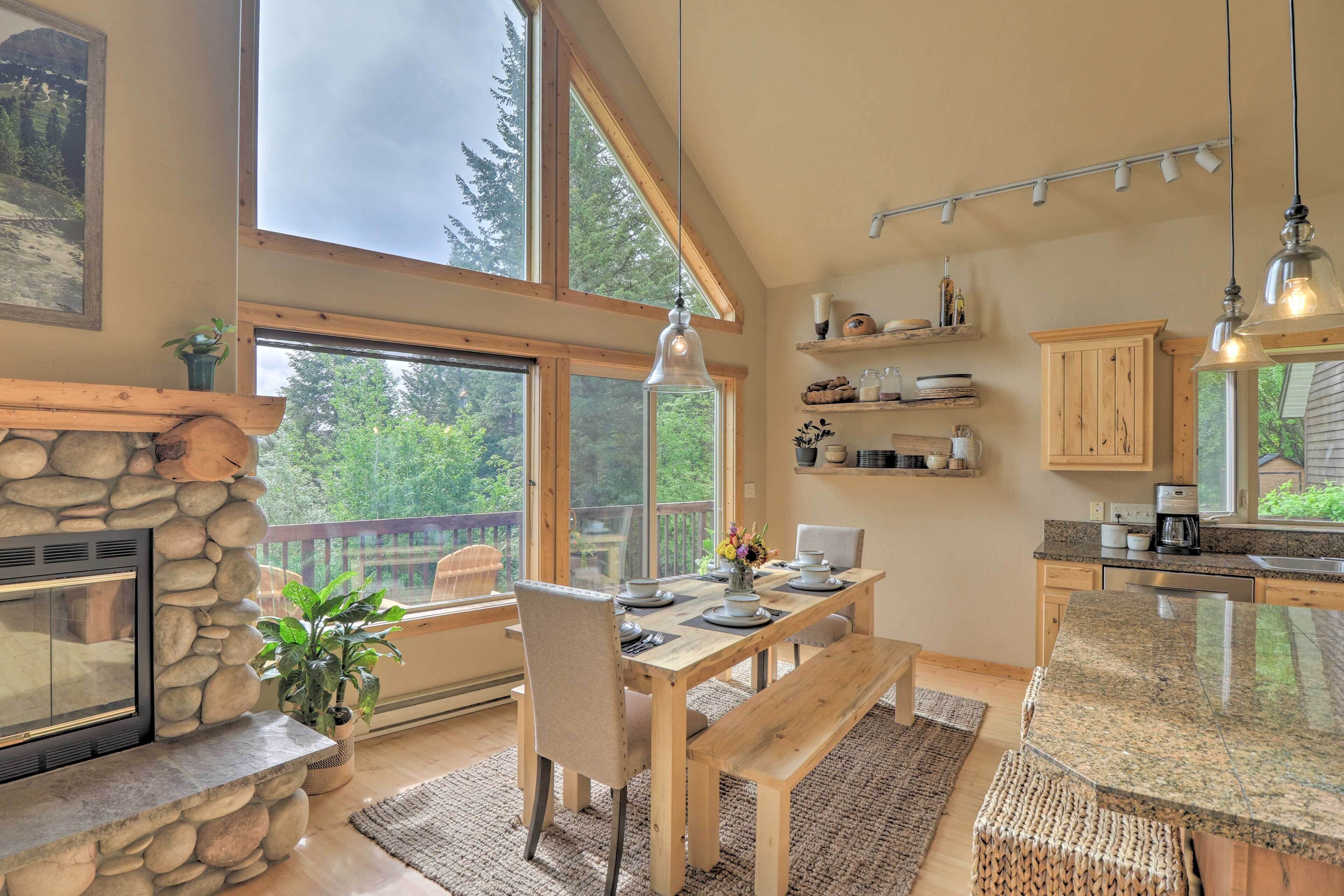 Una cocina amplia con chimenea de piedra, mesa de comedor de madera y grandes ventanales con vistas al exterior.