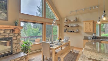 Una cocina amplia con chimenea de piedra, mesa de comedor de madera y grandes ventanales con vistas al exterior.