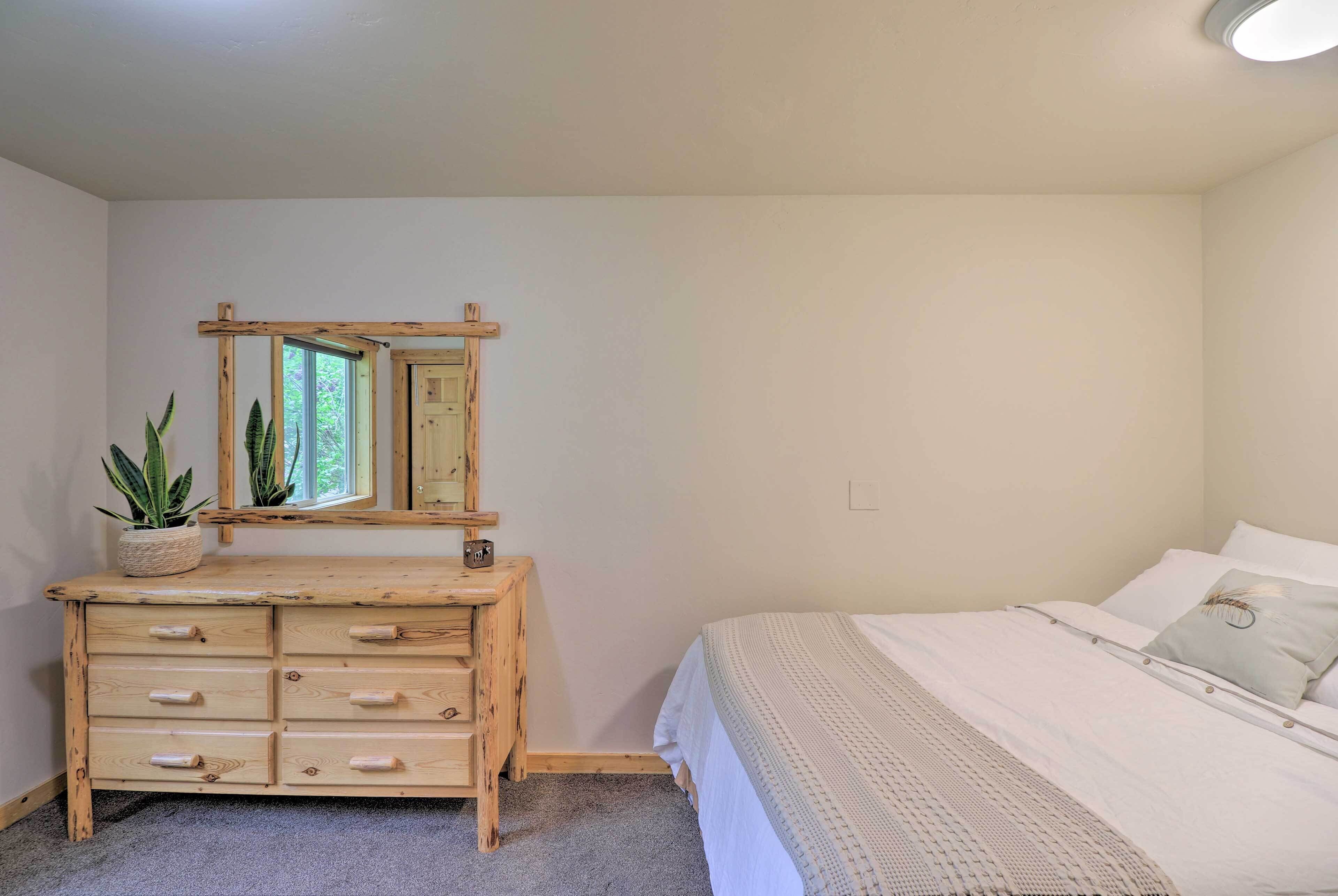 Un dormitorio con cómoda de madera, cama con ropa de cama blanca, espejo y planta en maceta.