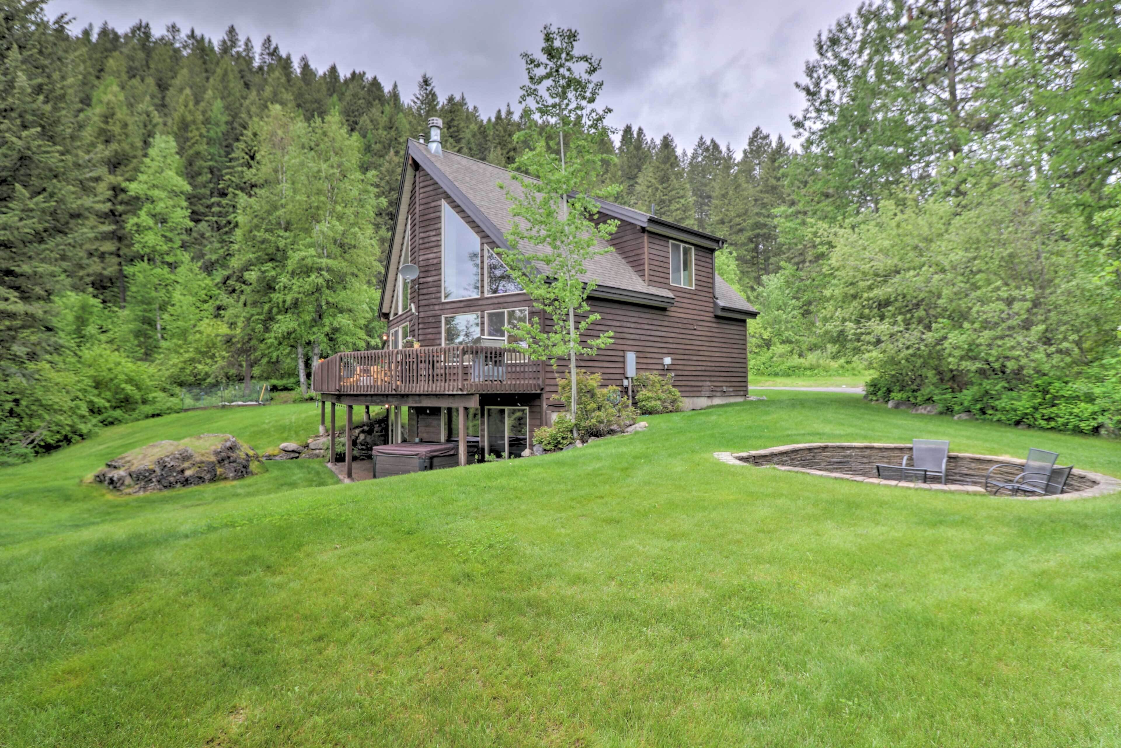A modern house with a deck, surrounded by a well-maintained lawn and dense forest.