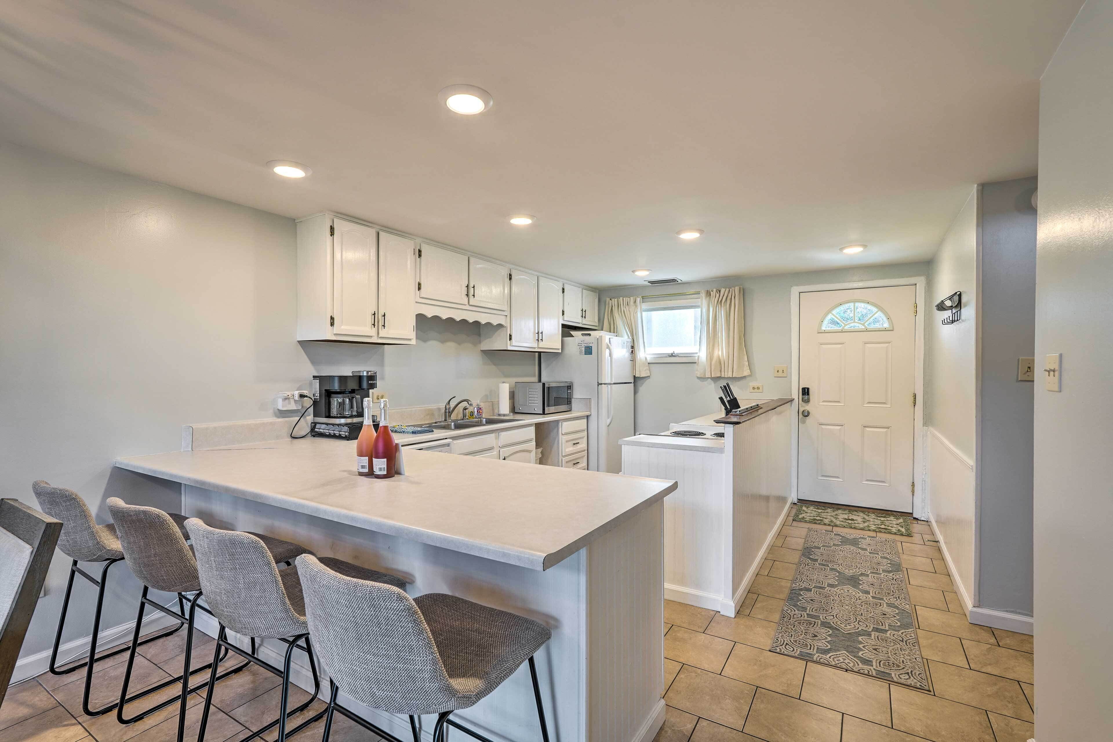 A modern kitchen with white cabinets, a central island with bar stools, a microwave, and a refrigerator.