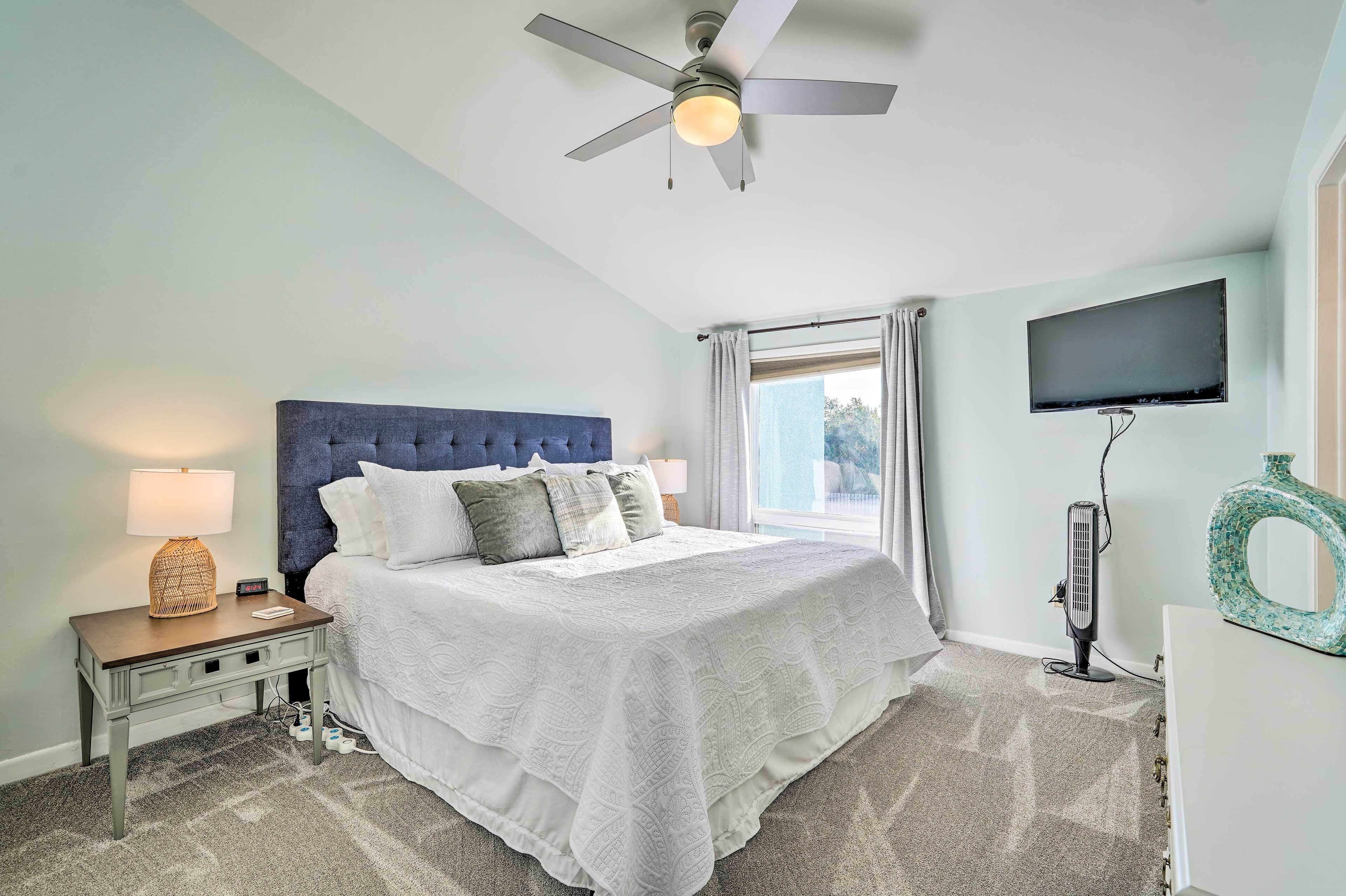 A bedroom with a bed, a nightstand, a ceiling fan, a TV, and a window with curtains.