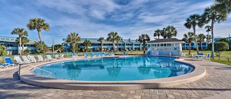 A pool area with lounge chairs and palm trees, surrounded by a building with a blue facade.