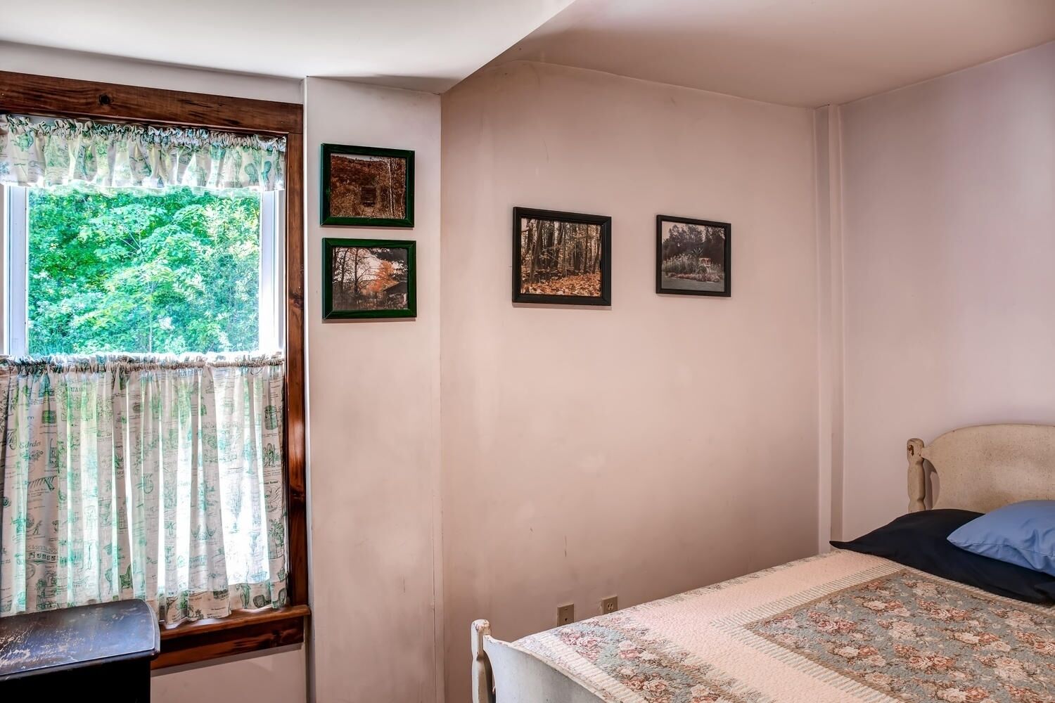 A bedroom with a bed, a window with curtains, and three framed pictures on the wall.