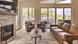 A modern living room with a fireplace, leather sofa, and large windows offering mountain views.