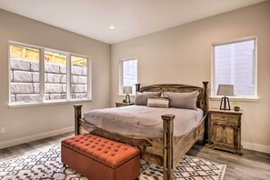 A bedroom with a large bed, two bedside tables, a wooden headboard, and a window with a stone-like view.
