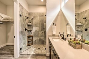 A modern bathroom with a glass-enclosed shower, a vanity with a large mirror, and a wooden shelf with plants.