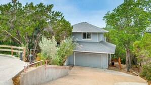 A two-story house with a garage, surrounded by trees and a concrete driveway. - Beach & Pool Access at Lake Travis Family Getaway! (Leander)