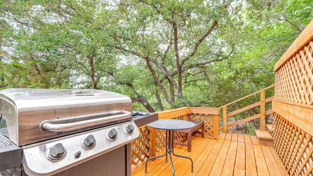 A wooden deck with a grill and a table, surrounded by trees. - Beach & Pool Access at Lake Travis Family Getaway! (Leander)