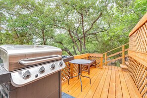A wooden deck with a grill and a table, surrounded by trees. - Beach & Pool Access at Lake Travis Family Getaway! (Leander)