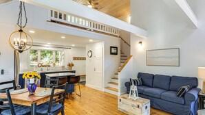 A spacious living area with a wooden floor, a blue sofa, a dining table with chairs, and a kitchen in the background. - Sunny Stockton Springs Home < 1 Mi to Beach! (Stockton Springs)