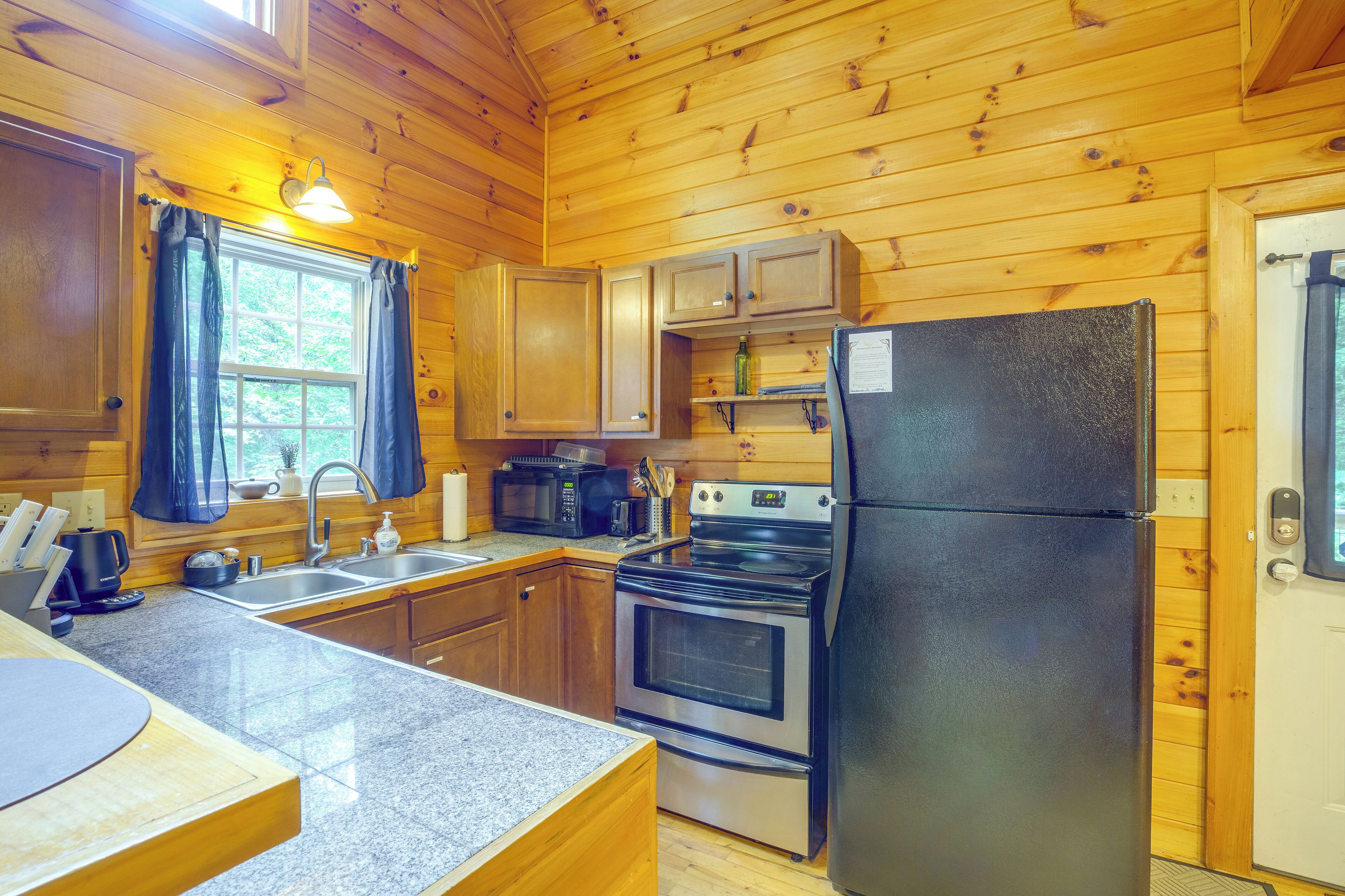 A compact kitchen with wooden walls, a stainless steel refrigerator, a microwave, an oven, and a sink.