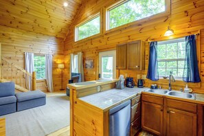 Interior de una cabaña de madera con cocina, comedor y una escalera.