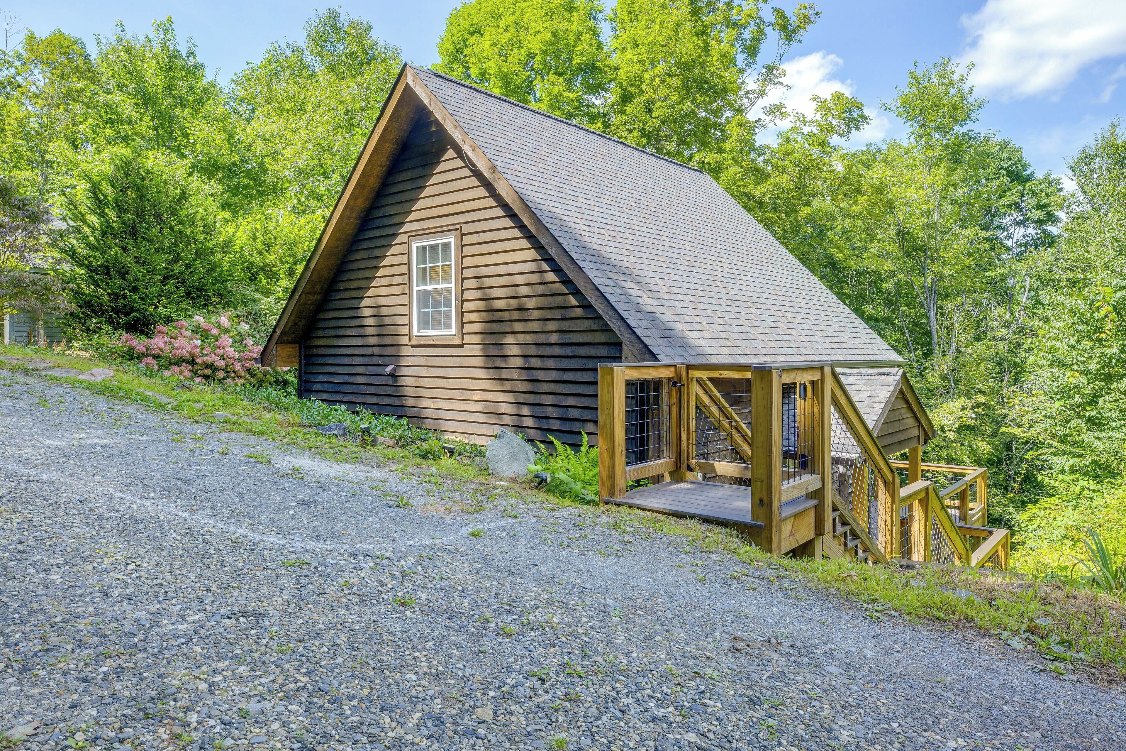 A wooden cabin with a pitched roof, a small porch, and a gravel driveway.