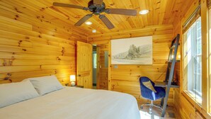 Une pièce de style cabane en bois, comprenant un lit, un bureau, une chaise, un ventilateur de plafond et un tableau accroché au mur.