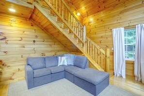 Interior de madera con una escalera, un sofá seccional gris y una ventana con cortinas.